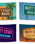 Set of four “Butt Stuff Blvd” flags featuring different designs — street sign style, beach sunset with palm trees, neon lights, and vintage marquee — funny dorm flags for college partiers from CollegeWares.