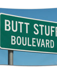 Green highway-style sign flag with white text reading “Butt Stuff Boulevard” against a blue sky — funny adult humor dorm flag for college students from CollegeWares.