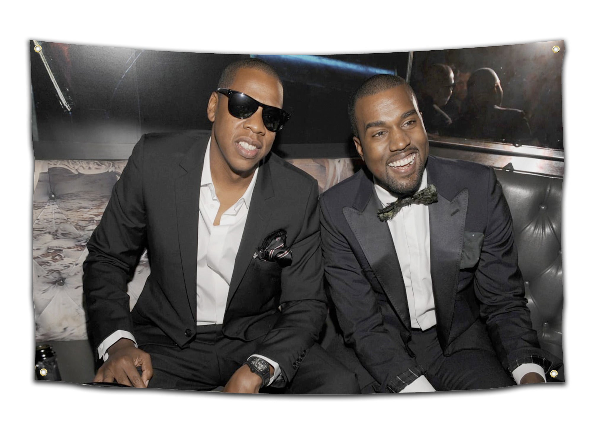 Flag featuring Kanye West and Jay-Z wearing black suits, sunglasses, and bow ties, smiling and sitting on a black leather couch — rapper duo flag from CollegeWares.