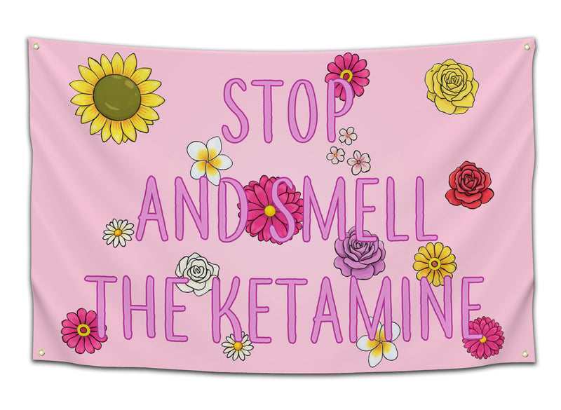 Pink floral flag featuring colorful cartoon flowers and bold purple text that reads “STOP AND SMELL THE KETAMINE” — funny dorm flag for stoners, rave kids, and meme lovers as chaotic college party wall decor from CollegeWares.